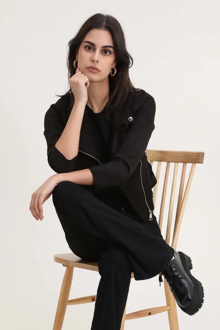 Modèle féminine assise, portant un perfecto noir, exprimant style et élégance, sur une chaise en bois.