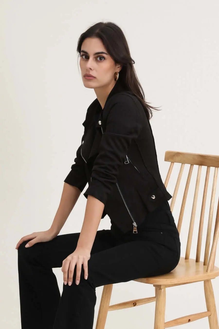 Femme portant un perfecto noir, assise sur une chaise en bois, style moderne et élégant.